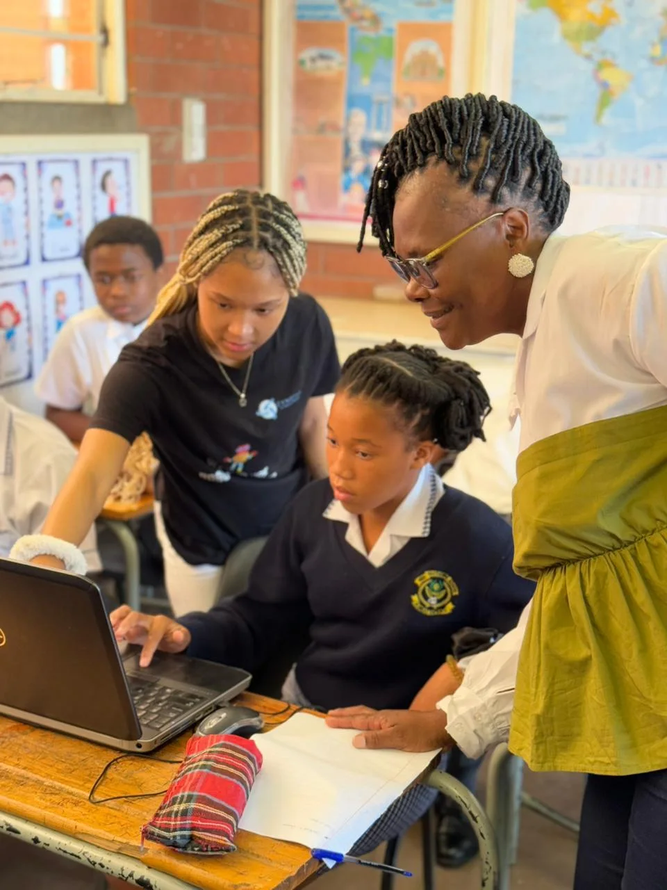 A facilitator supporting learners working at a laptop in a classroom